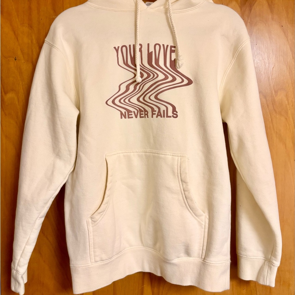 LOVE NEVER FAILS CREAM UNISEX HOODIE